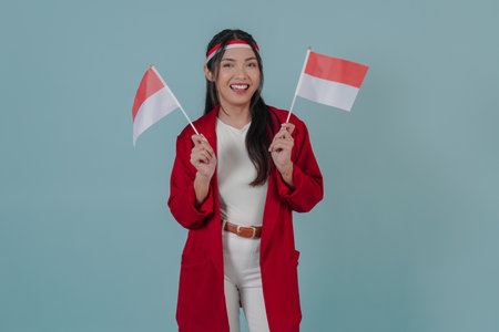 Happy Indonesian woman wearing a red coat and white pants is raising two flags while smiling. Indonesia Independence Day concept.の写真素材