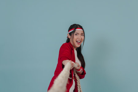 Young Indonesian woman in a red jacket is pulling on a rope, joining competition for Indonesian Independence Day.の写真素材