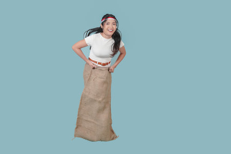 Happy Indonesian woman wearing gunny sack and jumping, joining competition. Indonesia Independence Day concept.の写真素材