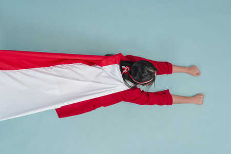 Young Indonesian woman wearing country flag on her back and raising hands superhero flying gesture. Indonesia Independence Day concept.の写真素材
