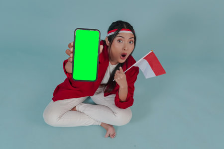 Young Indonesian woman is showing copy space on her phone with shocked expression while sitting down...