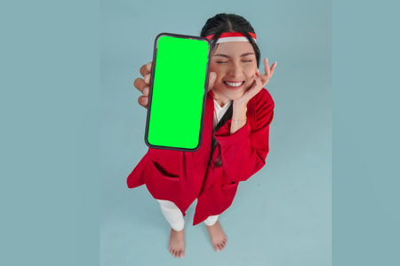 Attractive young Indonesian woman smiling while showing copy space on her phone screen to the camera. Indonesia Independence Day concept.の写真素材