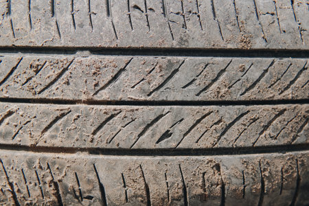 A tire with a lot of dirt on it. The tire is old and worn on the ground.