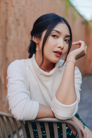 Beautiful young woman in a green sequined skirt stands in front of a brick wall. She is wearing a white shirt and heels.の写真素材