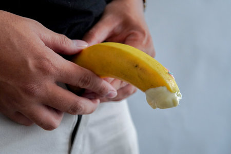 A man is holding a banana with creamy texture on the tip of the fruit.の写真素材