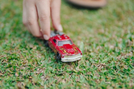 Close up of a boy's hand is holding a red toy car on a grassy field. The scene is calm and fun, the kid playing in outdoor park enjoying scenery.の写真素材