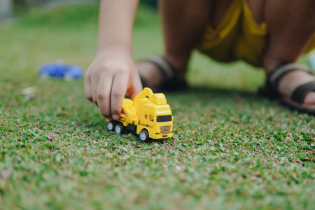 Close up of a boy's hand is holding a yellow truck toy on a grassy field. The scene is calm and fun, the kid playing in outdoor park enjoying scenery.の写真素材