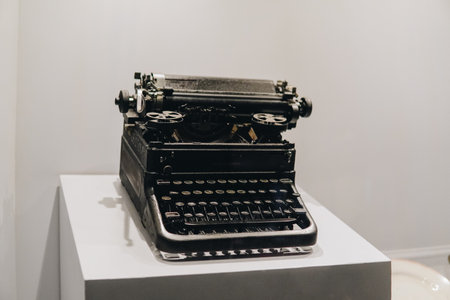 An old fashioned typewriter sits on a white pedestal. The typewriter is black and has a vintage look...