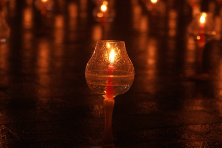 Close up portrait of oil candle lit in a glass vase. The candle is surrounded by other candles, creating a warm and cozy atmosphere.の写真素材
