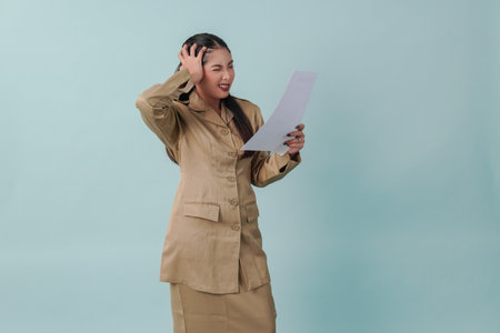 Annoyed government worker woman wearing khaki uniform holding document paper with stressful and mad expression. PNS civil servant concept.の写真素材