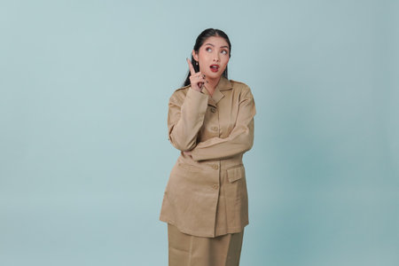 Thoughtful Indonesian government worker woman wearing khaki uniform pointing to the copy space upward finding idea.の写真素材