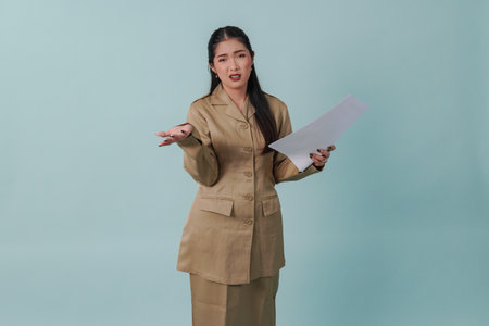 Beautiful Indonesian government worker woman wearing khaki uniform holding a document report with a confused expression. PNS civil servant concept.の写真素材