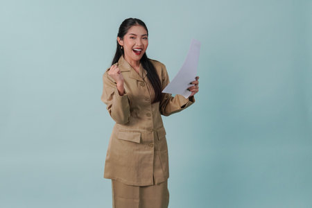 Cheerful Indonesian government worker woman wearing khaki uniform holding a document paper with a happy successful expression. PNS civil servant concept.の写真素材