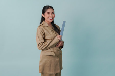 A young beautiful Indonesian government worker with khaki uniform bringing document and smiling to the camera. PNS and civil servant concept.の写真素材