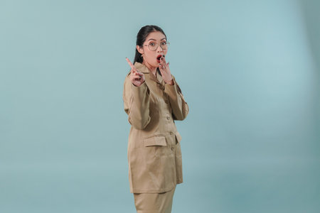 Surprised government worker woman wearing khaki uniform and glasses pointing to the copy space behind her.の写真素材