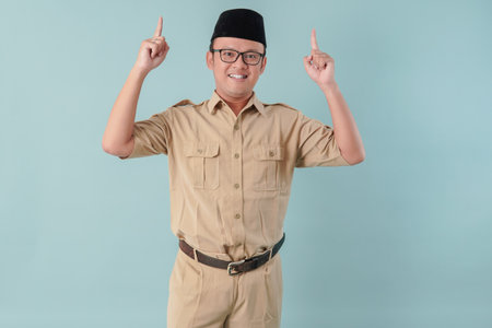 Smiling Indonesian government worker man wearing khaki uniform pointing to the copy space upwards....