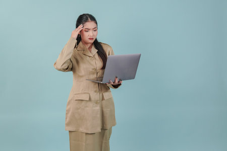 Confused government worker woman holding her laptop looking serious, isolated by blue background. PNS civil servant concept.の写真素材