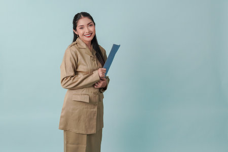 A young beautiful Indonesian government worker with khaki uniform bringing document and smiling to the camera. PNS and civil servant concept.の写真素材