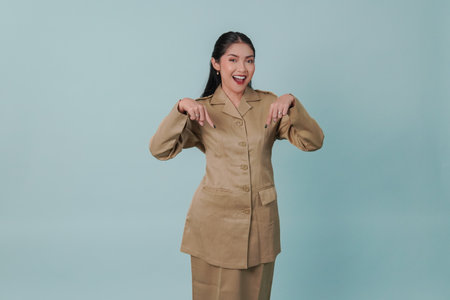 Smiling Indonesian government worker woman wearing khaki uniform pointing to the copy space downward. PNS civil servant concept.の写真素材