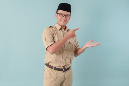 Happy Indonesian government worker man wearing khaki uniform pointing to the copy space beside him....