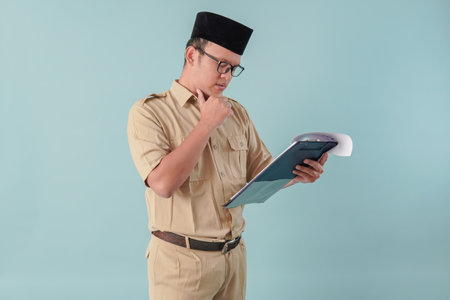 Thoughtful government worker man wearing khaki uniform holding document paper feeling confused. PNS civil servant concept.の写真素材