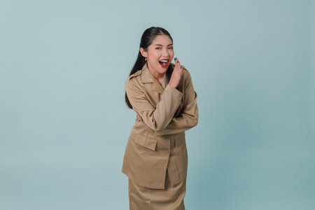 Joyful Indonesian government worker woman is shouting or yelling isolated by a blue background.の写真素材