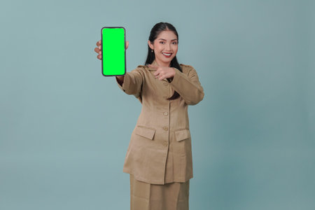 Joyful Indonesian government worker woman wearing khaki uniform presenting copy space on her phone. PNS civil servant concept.の写真素材
