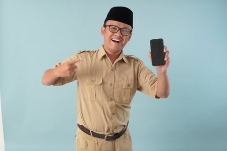 Excited Indonesian government worker man wearing khaki uniform presenting copy space on his smartphone. PNS civil servant concept.の写真素材