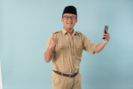 Indonesian government worker man wearing khaki uniform doing video call with a happy successful expression. PNS civil servant concept.の写真素材