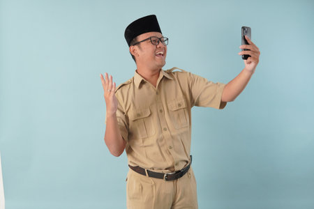 Joyful government worker man wearing khaki uniform while doing video call using smartphone. PNS civil servant concept.の写真素材