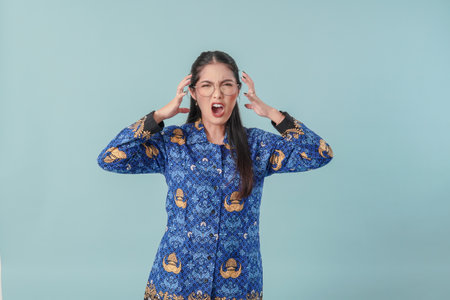 Frustrated Indonesian government worker woman wearing blue batik uniform feeling angry and is...