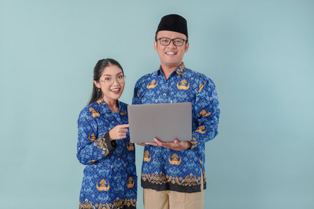 Two happy Indonesian government workers couple wearing blue batik uniform, holding and pointing to...