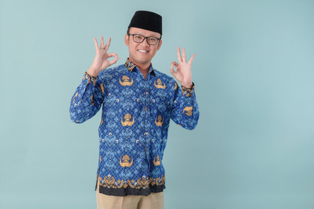 Smiling government worker man wearing blue batik uniform giving OK finger gesture. PNS civil servant...