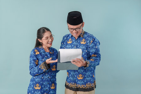 Two Indonesian government workers wearing blue batik uniform and holding a document, discussing...