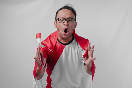 Funny looking Indonesian man holding their country flag while raising fist to celebrate something. Indonesia Independence Day and sport concept.の写真素材