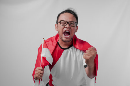 Funny looking Indonesian man holding their country flag while raising fist to celebrate something. Indonesia Independence Day and sport concept.の写真素材