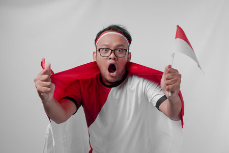 Funny looking Indonesian man holding their country flag while raising fist to celebrate something. Indonesia Independence Day and sport concept.の写真素材