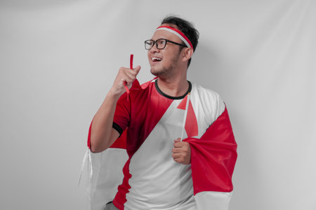 Excited young Indonesian man holding a mini flag with a happy successful expression. Indonesia Independence Day and sport concept.の写真素材