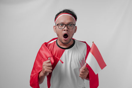 Funny looking Indonesian man holding their country flag while raising fist to celebrate something. Indonesia Independence Day and sport concept.の写真素材