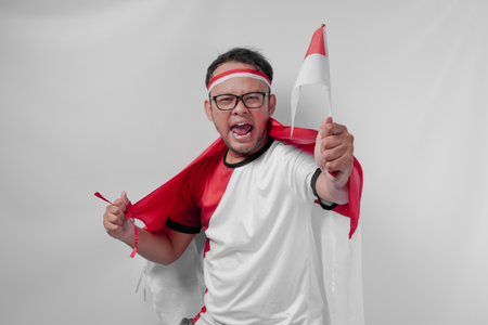 Funny looking Indonesian man holding their country flag while raising fist to celebrate something. Indonesia Independence Day and sport concept.の写真素材
