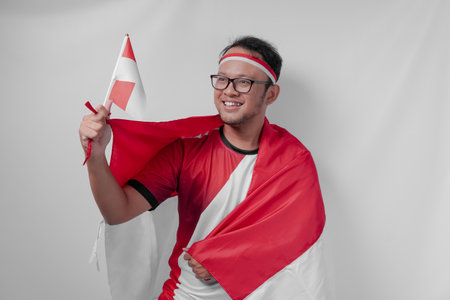 Excited young Indonesian man holding a mini flag with a happy successful expression. Indonesia Independence Day and sport concept.の写真素材