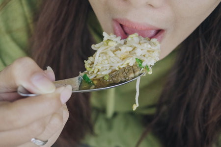 Close up portrait of Asian woman using spoon to eat Indonesian traditional cuisine named soto soup mainly composed of broth, meat, and vegetables.の写真素材