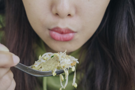 Close up portrait of Asian woman using spoon to eat Indonesian traditional cuisine named soto soup mainly composed of broth, meat, and vegetables.の写真素材