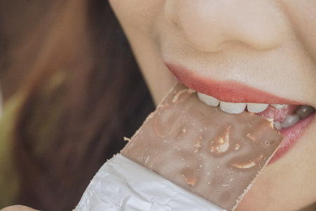 Close up portrait of Asian woman eating a chocolate bar while smiling as she enjoys her snack.の写真素材