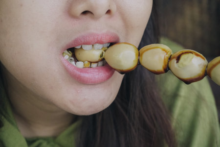 Close up portrait of Asian woman eating a skewer made from quail eggs poured by soy sauce on top.の写真素材