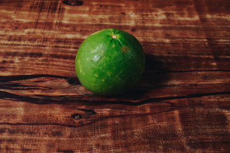 A green lime citrus fruit (Citrus aurantiifolia) placed on top of a wooden table.