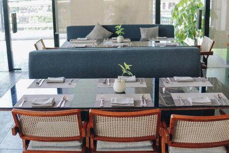 A black dining table with a vase of green plant and silverware is being set up for a meal inside a restaurant.の写真素材