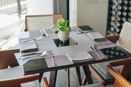 A black dining table with a vase of green plant and silverware is being set up for a meal inside a restaurant.の写真素材