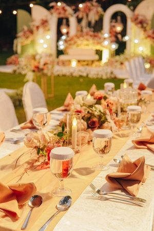 Night dinner long table with white table cloth and an elegant floral arrangement in the middle, set up for a wedding or a special event.の写真素材