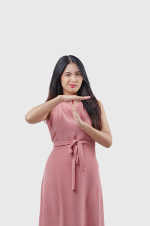 Cute young Asian woman wearing pink dress doing time out gesture with hands and serious face, isolated white background.の写真素材
